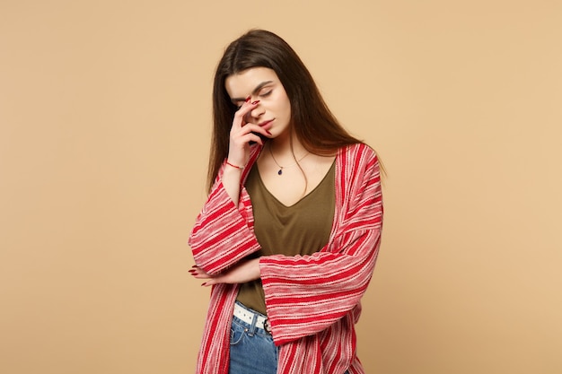 Ritratto di una giovane donna stanca in abiti casual che tiene gli occhi chiusi, mettendo la mano sul viso isolato su sfondo beige pastello in studio. Persone sincere emozioni, concetto di stile di vita. Mock up copia spazio.