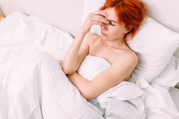 Ritratto di una giovane donna triste e stanca sdraiata a letto malattia e mal di testa