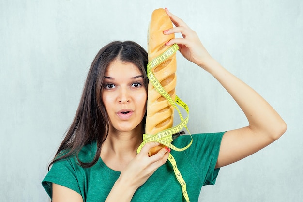 Ritratto di una giovane e bella donna bruna affamata che tiene un panino ad alto contenuto calorico con un nastro di misurazione concetto di dieta e rifiuto di cibo dannoso malsano