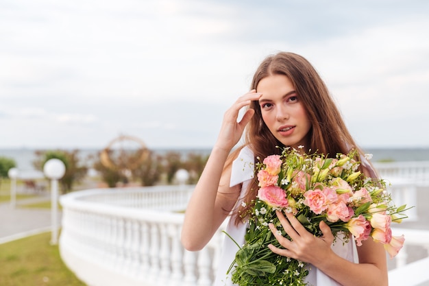 Ritratto di una giovane e bella donna che tiene un mazzo di fiori in piedi su una terrazza all'aperto