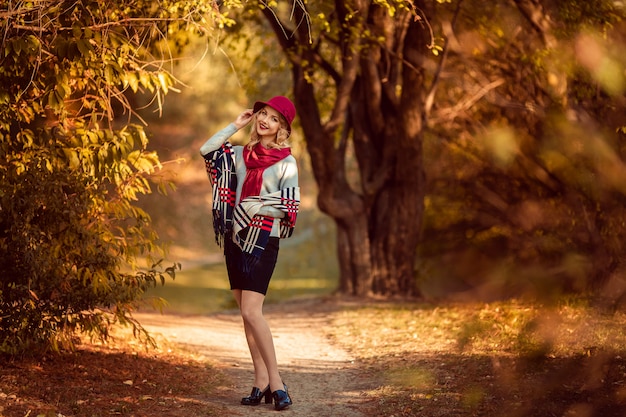 Ritratto di una giovane e bella donna in un cappello bordeaux in autunno in una passeggiata nel parco