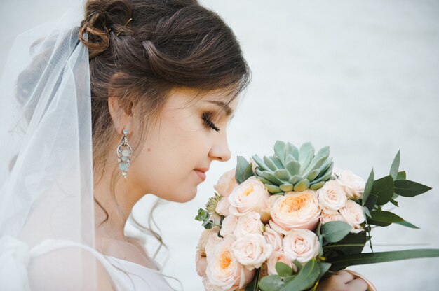 Ritratto di una giovane e bella sposa con un bouquet su uno sfondo bianco. Nozze.