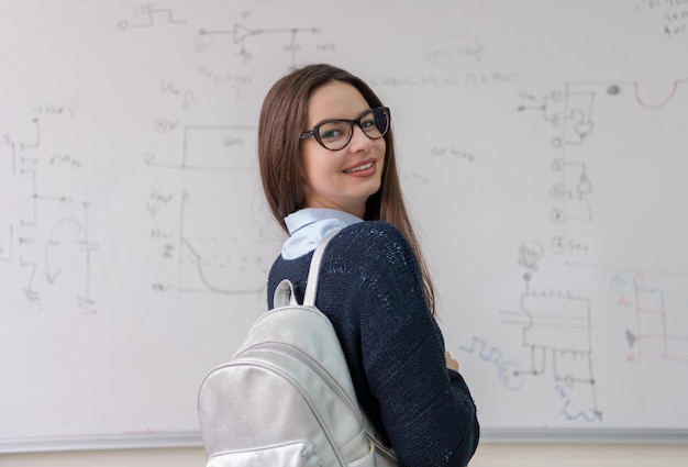 ritratto di una giovane e bella studentessa in piedi davanti alla lavagna bianca e guardando la telecamera