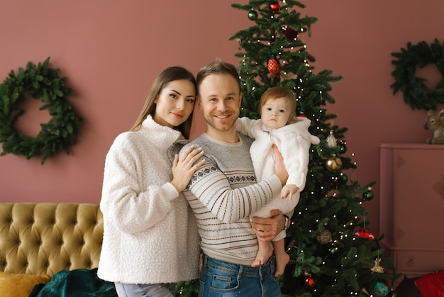 Ritratto di una giovane famiglia alla moda con un bambino piccolo vicino all'albero di Natale nel soggiorno nella loro nuova casa