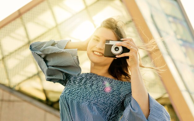 Ritratto di una giovane fotografa bionda in un vestito con una fotocamera retrò all'aperto