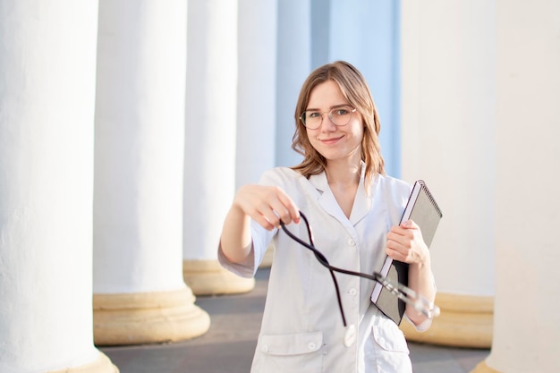 Ritratto di una giovane infermiera studentessa universitaria di medicina sta con fonendoscopio e documenti felice medico femminile in uniforme vicino all'ospedale