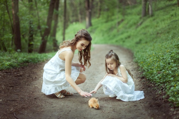 Ritratto di una giovane madre con sua figlia nella foresta con un piccolo coniglio