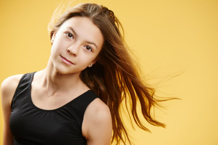 Foto ritratto di una giovane ragazza adolescente dai capelli castani su sfondo giallo