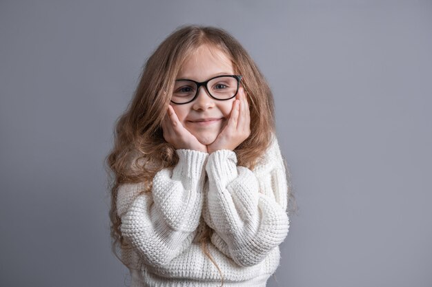 Ritratto di una giovane ragazza attraente con lunghi capelli biondi fluenti in un maglione bianco sorridente su uno sfondo grigio studio. Copia spazio.