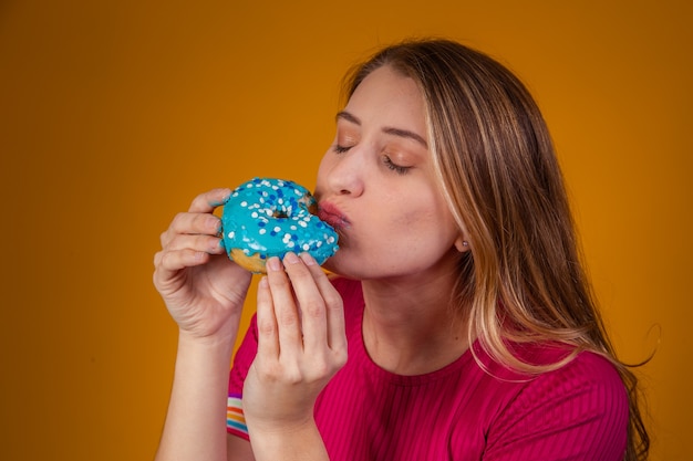 Ritratto di una giovane ragazza bionda che mangia deliziose ciambelle colorate.