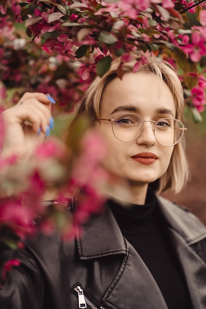 Ritratto di una giovane ragazza bionda con gli occhiali accanto all'albero con foglie rosse in autunno