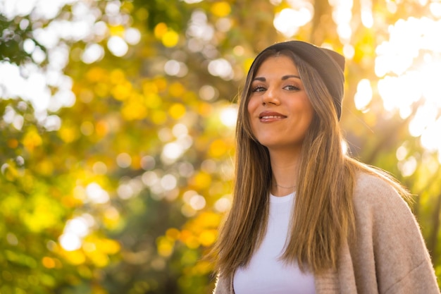 Ritratto di una giovane ragazza bionda con un cappello di lana in autunno che cammina nel parco al tramonto