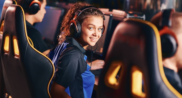 Ritratto di una giovane ragazza di razza mista felice, giocatrice che indossa le cuffie che sorride alla telecamera mentre gioca ai videogiochi online, partecipando al torneo eSport. Team di professionisti del cybersportsport