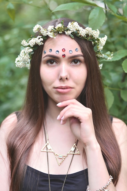 Ritratto di una giovane ragazza emotiva con una corona di fiori sulla sua testa e ornamenti lucidi sulla sua fronte