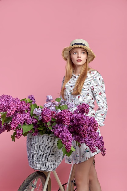 Ritratto di una giovane ragazza felice con bicicletta vintage e fiori su sfondo rosa.