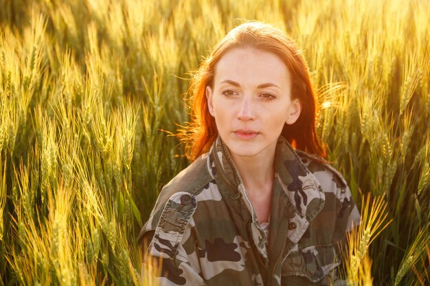 Ritratto di una giovane ragazza felice seduta su un raccolto di grano dorato in un campo giallo al tramonto