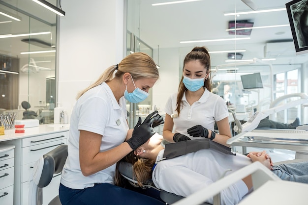 Ritratto di una giovane ragazza in una sedia dentale che viene trattata da un dentista femminile e da un assistente femminile per il trattamento della carie dei denti sani