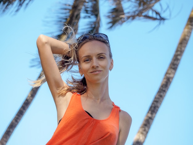 Ritratto di una giovane ragazza in vacanza in una maglia arancione e occhiali da sole su un'isola tropicale. soffia una forte brezza dall'oceano