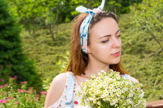Ritratto di una giovane ragazza premurosa che tiene in mano un grande mazzo di piccoli fiori bianchi mentre si trova nel parco