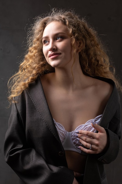 Ritratto di una giovane ragazza sexy riccia dai capelli rossi in una giacca con i capelli lunghi in studio Mostra i suoi seni sinuosi in un reggiseno