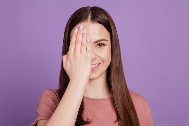 Ritratto di una giovane ragazza sorridente che copre metà del viso con la mano isolata su sfondo viola