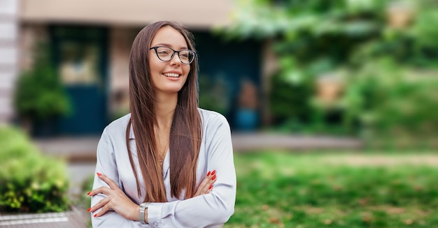 Ritratto di una giovane ragazza sorridente con gli occhiali sullo sfondo della facciata dell'edificio degli alberi della natura