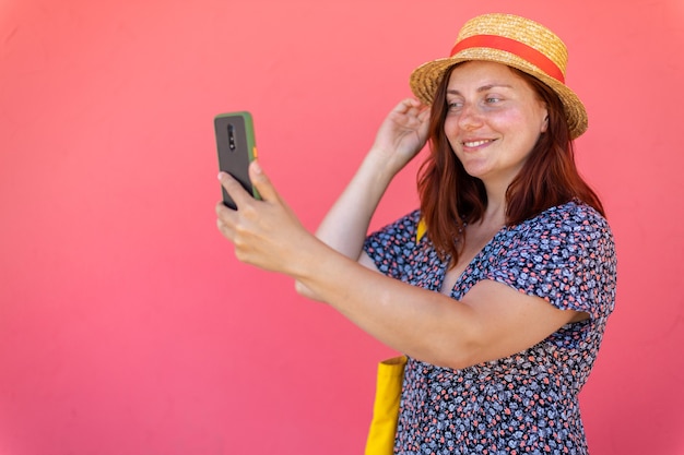 Ritratto di una giovane ragazza sorridente in un cappello di paglia e un vestito prendendo un selfie