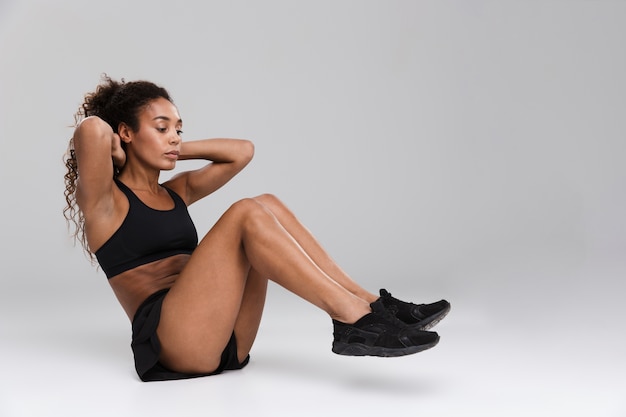 Ritratto di una giovane sportiva afro americana forte facendo esercizi addominali isolate su uno sfondo grigio