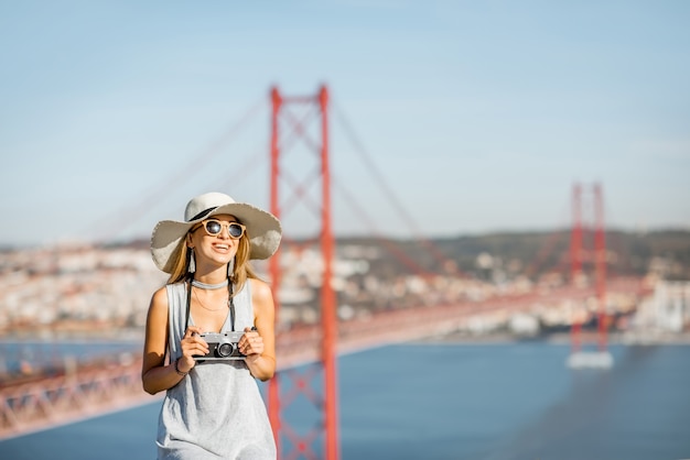 Ritratto di una giovane turista con macchina fotografica seduta sullo sfondo della vista del paesaggio con un bellissimo ponte di ferro nella città di Lisbona, Portogallo