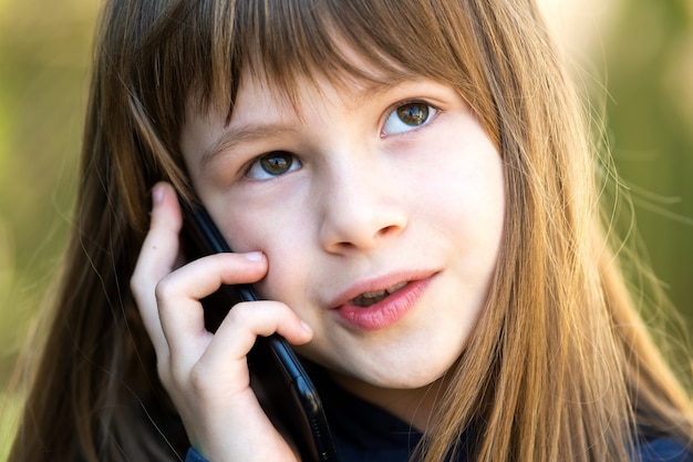 Ritratto di una graziosa bambina con i capelli lunghi che parla al cellulare