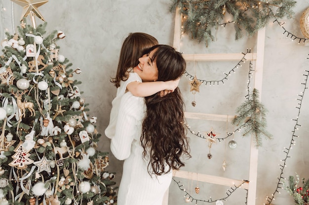 Ritratto di una madre e di una figlia gioiose sullo sfondo degli interni di Natale. Vacanze invernali. la mamma tiene il bambino in braccio e si abbracciano