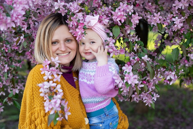 Ritratto di una madre e la sua piccola figlia sullo sfondo di un albero in fiore in primavera.