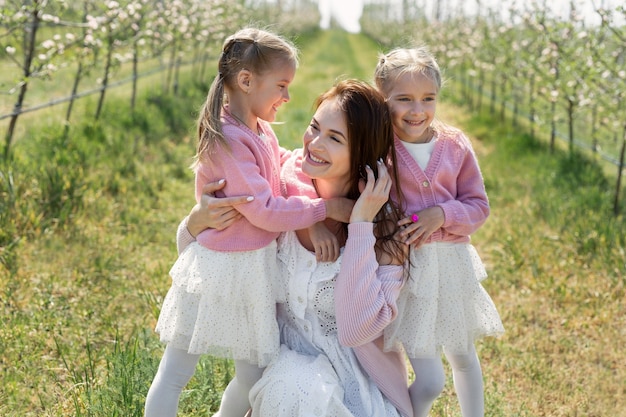 Ritratto di una madre e le sue figlie gemelle in un frutteto di mele in fiore.