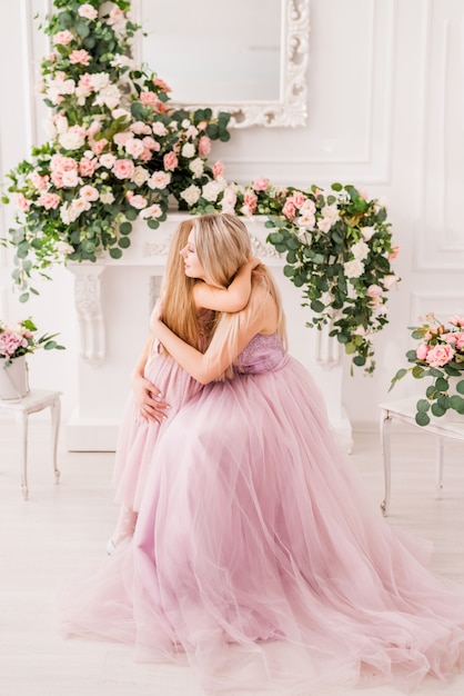 Ritratto di una madre e una figlia in abiti eleganti in un bellissimo interno con fiori.