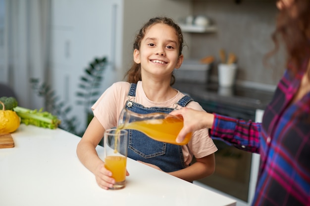 Ritratto di una mamma versa il succo d'arancia a sua figlia ridente per colazione