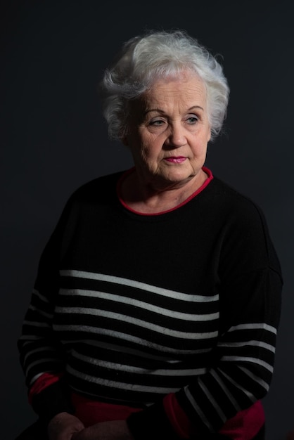 Ritratto di una nonna con un maglione scuro su sfondo scuro
