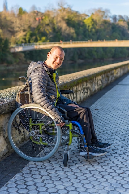 Ritratto di una persona disabile in sedia a rotelle che sorride accanto a un fiume in un parco