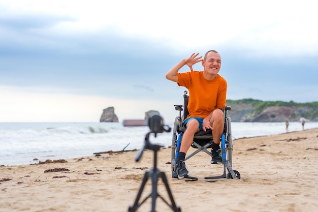 Ritratto di una persona disabile in sedia a rotelle sulla spiaggia che registra un video