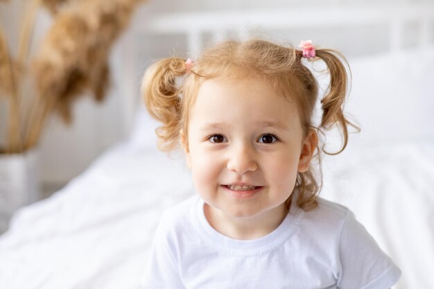 ritratto di una piccola bambina bionda e carina su un letto di cotone bianco a casa felice sorridente bambino in primo piano