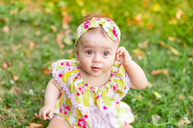 Ritratto di una piccola bambina di 7 mesi seduto sull'erba verde in un vestito giallo