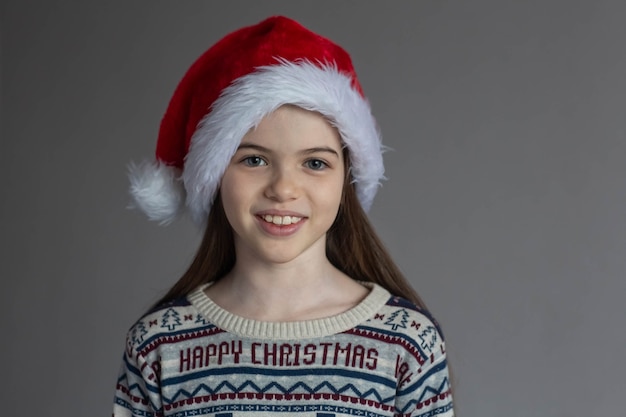 Ritratto di una piccola bella ragazza sorridente in un maglione di Capodanno e un concetto di pubblicità del cappello della Santa