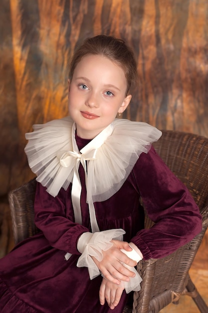 Ritratto di una piccola principessa in un abito classico bordeaux con una balza in posa su uno sfondo vintage Una ragazza con capelli lunghi lucidi perfetti Stile retrò e alla moda Per chiudere Studio shot