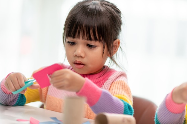 Ritratto di una piccola ragazza asiatica che taglia una carta nelle attività della classe fai-da-te a SchoolScissors taglia la carta