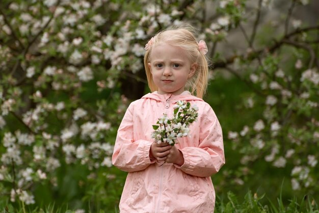 Ritratto di una piccola ragazza caucasica seria con un giardino floreale primaverile in una giornata di sole con un ramo in fiore