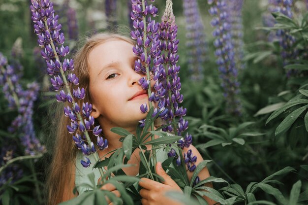 Ritratto di una piccola ragazza felice sveglia che gode dei lupini della fioritura