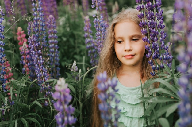 Ritratto di una piccola ragazza felice sveglia con i lupini della fioritura