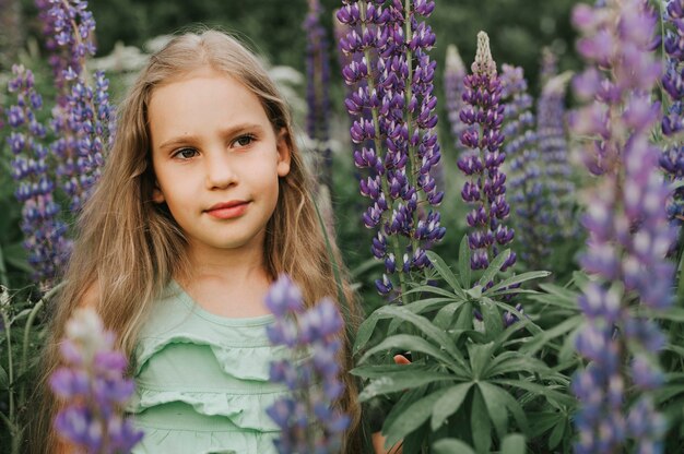 Ritratto di una piccola ragazza felice sveglia con i lupini della fioritura