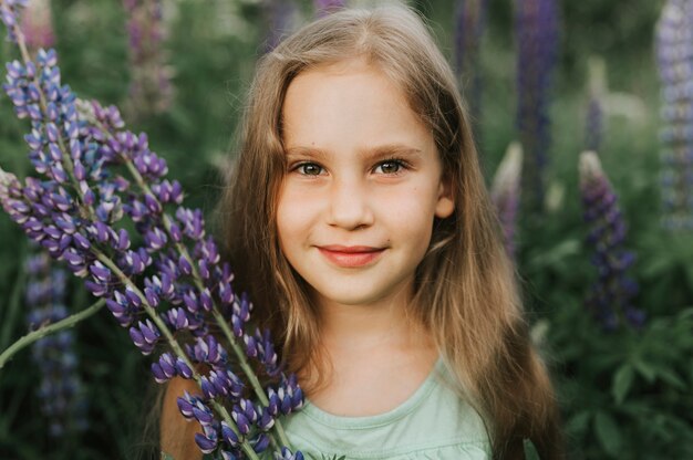 Ritratto di una piccola ragazza felice sveglia con i lupini della fioritura