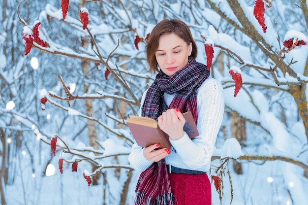 Ritratto di una ragazza affascinante che legge un libro nella foresta invernale.