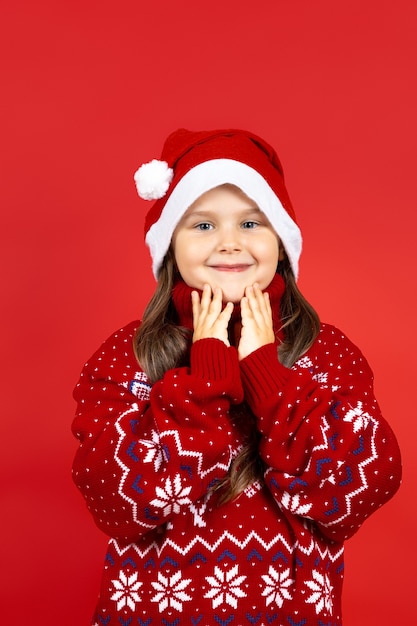 Ritratto di una ragazza affascinante sorridente con un maglione natalizio a maglia rossa con renne che si toccano il viso con...